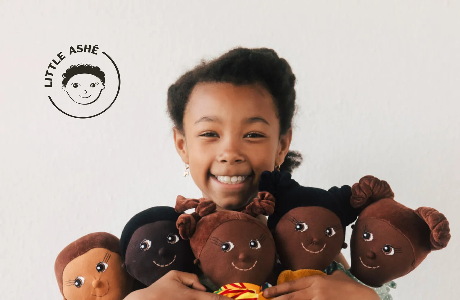A happy girl holding several LITTLE ASHÉ dolls in her hands and a LITTLE ASHÉ logo in the top-left